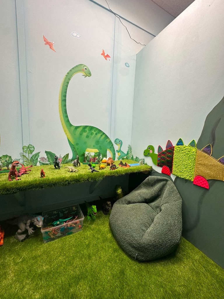 The dinosaur corner, with a long-necked mural, figurines on the grass shelf and a beanbag.