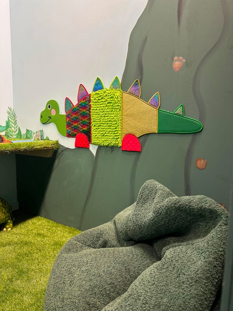 A close look at the textured stegosaurus sensory board, with a beanbag on the grass.