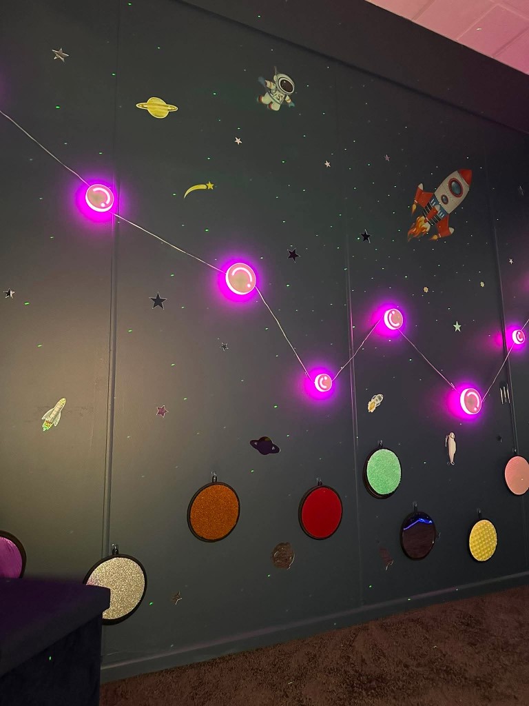 The space wall, with pink constellation lights, star stickers and tactile circular panels.