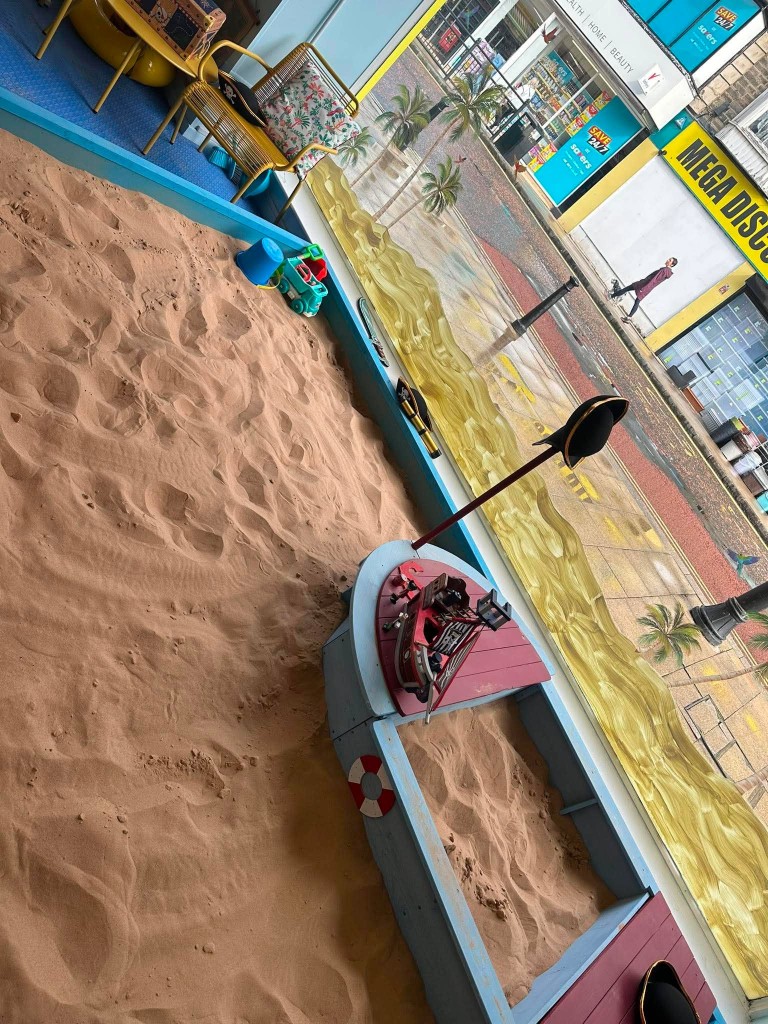 The wooden pirate boat in the sand pit, with Newgate Street through the window behind.