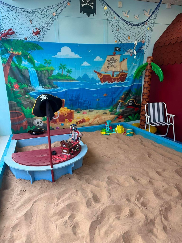 The sand pit boat with a pirate hat on the mast, buckets in the sand and an inflatable palm tree.