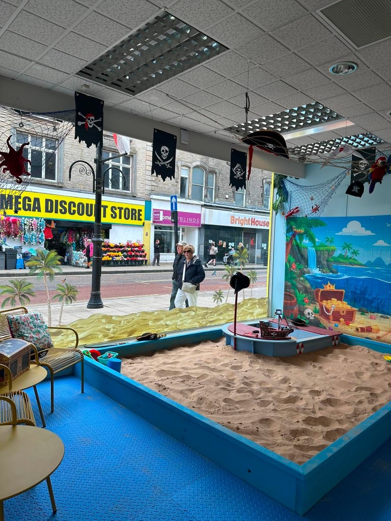 The pirate sand pit by the window, with yellow chairs for grown-ups looking on.
