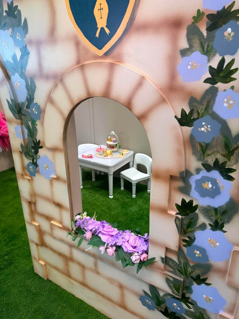 Looking through a castle arch at a tea party table on the grass, with flowers on the sill.