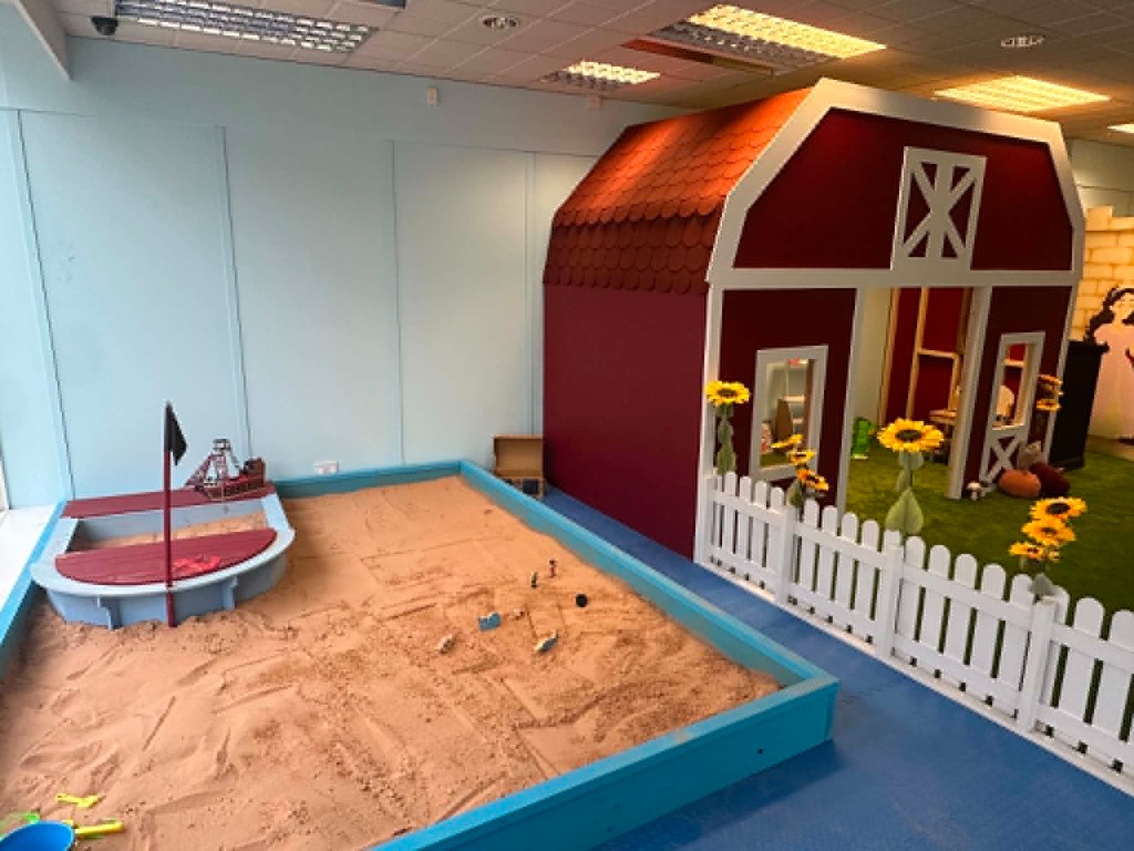 The red barn beside the sand pit, with sunflowers and a white picket fence.