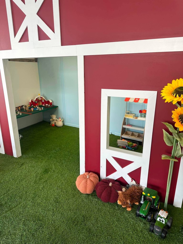 The red barn doorway, with toy tractors, a highland cow and the farm shop through the window.