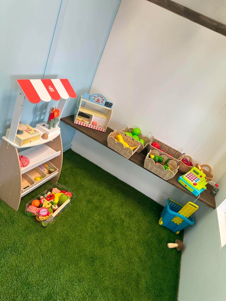 The little farm shop, with a striped awning, play fruit in baskets and a toy till.