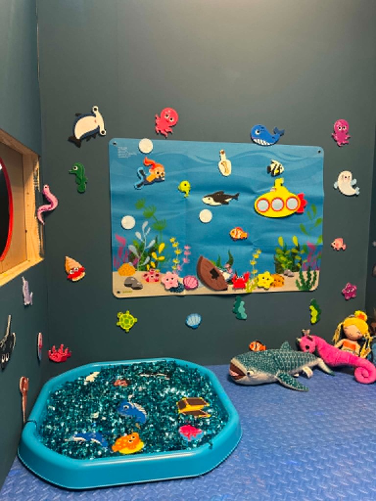 The under-the-sea sensory corner, with a wall of sea creatures and a tray of blue sensory play.